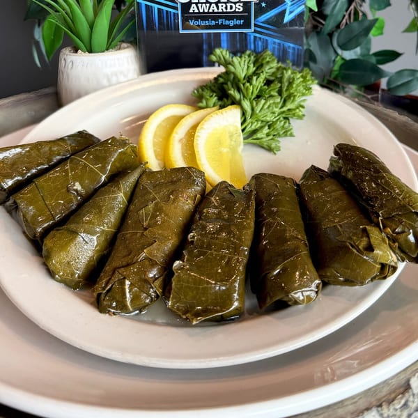 A white plate of Oliv Epicurean Grill's Mediterranean dolmades, garnished with lemon slices and parsley.