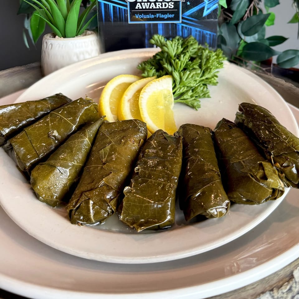 A white plate of Oliv Epicurean Grill's Mediterranean dolmades, garnished with lemon slices and parsley.