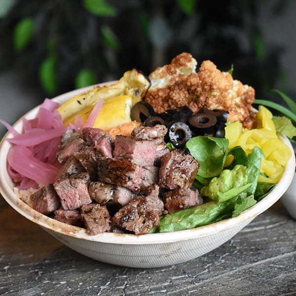 A Mediterranean bowl with steak, pickled onions, roasted cauliflower, olives, and greens.