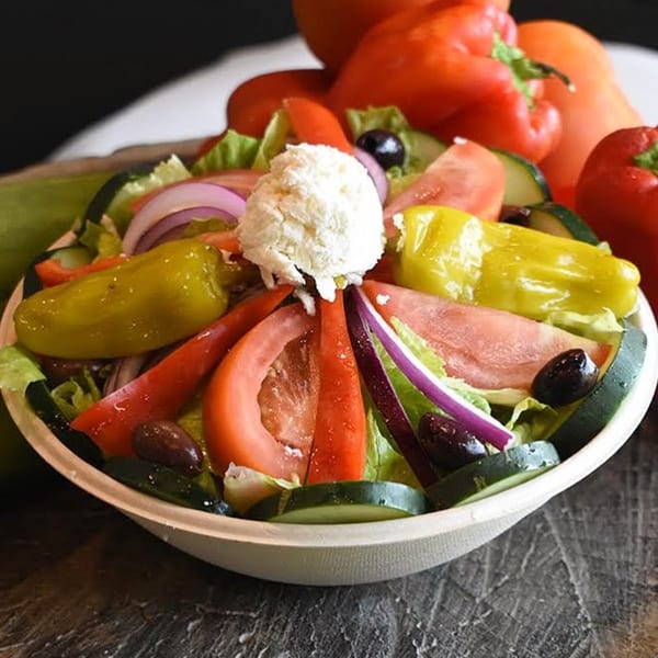 A vibrant Mediterranean salad with lettuce, tomatoes, cucumbers, onions, peppers, olives, and feta cheese.