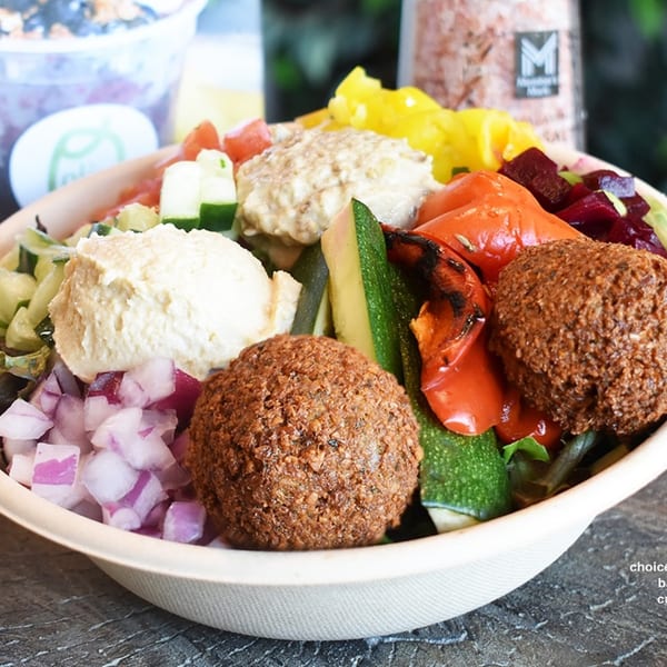 A Mediterranean bowl with falafel, hummus, roasted vegetables, and diced onions and cucumbers.