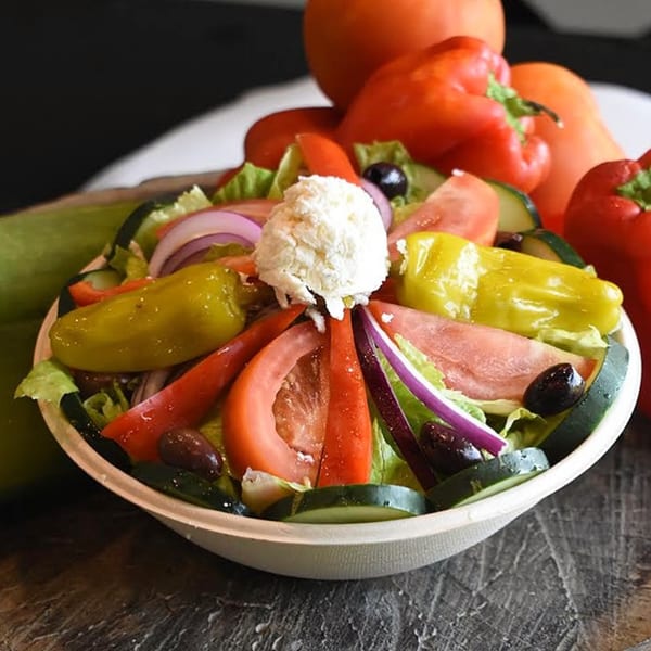 A vibrant Mediterranean salad with lettuce, tomatoes, cucumbers, onions, olives, peppers, and feta cheese.