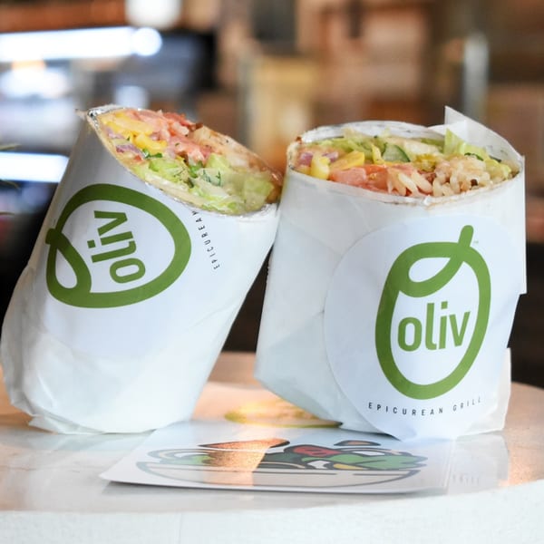 Two Oliv Epicurean Grill Mediterranean wraps, filled with fresh ingredients, stand upright on a counter.