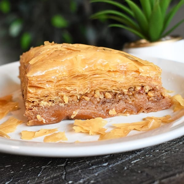 A golden-brown slice of baklava with flaky layers and a nutty filling on a white plate.