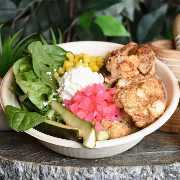 Mediterranean bowl with chicken, roasted cauliflower, spinach, corn, feta, pickled onions, and avocado.